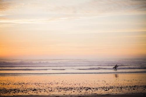 a person walking on the beach with a surfboard at Blue Kaouki Boutique Hotel in Sidi Kaouki