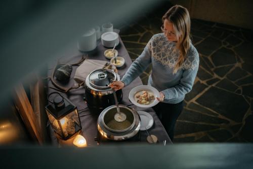 een vrouw die naast een tafel staat met een pot eten bij Lapland Hotels Ylläskaltio in Äkäslompolo