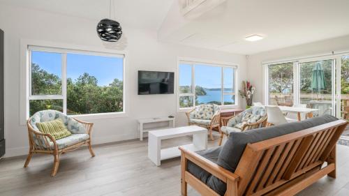 a living room with a couch and chairs and windows at Pohutukawa Paradise - Martins Bay Holiday Home in Mullet Point