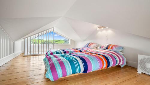 a bedroom with a bed with colorful sheets and a window at Pohutukawa Paradise - Martins Bay Holiday Home in Mullet Point