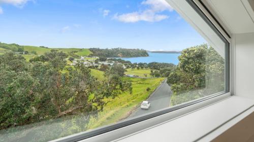 a window with a view of a road and a lake at Pohutukawa Paradise - Martins Bay Holiday Home in Mullet Point