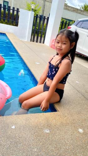 a little girl sitting next to a swimming pool at Sweet Party Hua-Hin Private Poolvilla From beach 3km in Hua Hin
