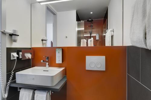 a bathroom with a white sink and an orange wall at Campanile Muenchen Sendling in Munich