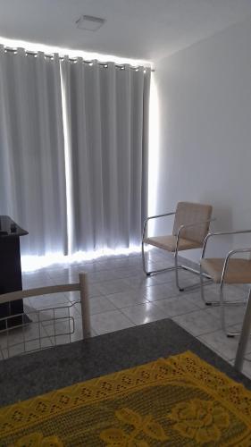 a living room with white curtains and chairs and a rug at Quarto em Apto ao lado Shopping in Cuiabá