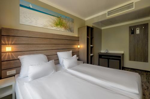 a bedroom with a large white bed with a wooden headboard at Tulip Inn München Messe in Munich