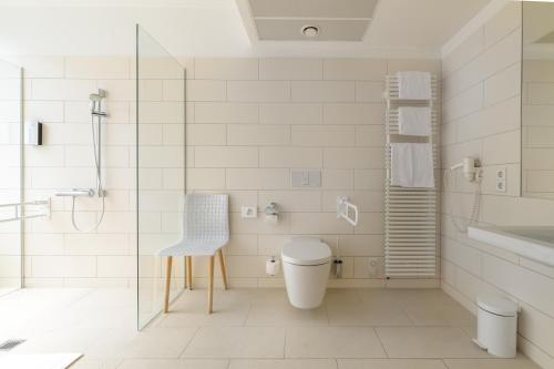 a bathroom with a shower and a toilet and a chair at Tulip Inn München Messe in Munich