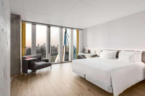 - une chambre blanche avec un grand lit et une chaise dans l'établissement nhow Rotterdam, à Rotterdam