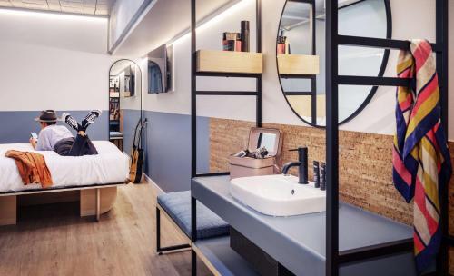 a man sitting on a bed in a room with a sink at LyLo Auckland in Auckland