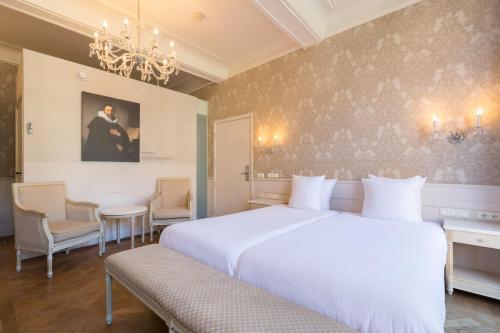 a bedroom with a large white bed and a chandelier at Amrâth Hotel Bigarré in Maastricht