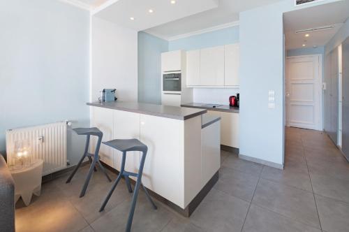 - une cuisine avec des placards blancs et 2 tabourets dans l'établissement Palais Miramar - Suite Blue Room - Vue Mer -Croisette Emplacement Unique - 20M Plage - WIFI - Clim, à Cannes