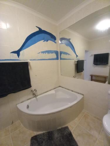 uma casa de banho com banheira e dois golfinhos pintados na parede em Dolphin Den em Port Shepstone