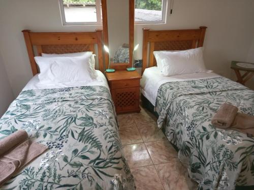 a bedroom with two beds and a table and two windows at Dolphin Den in Port Shepstone