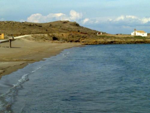 a beach with a house on a hill next to the water at Alegria Villas Complex in Vasilikos