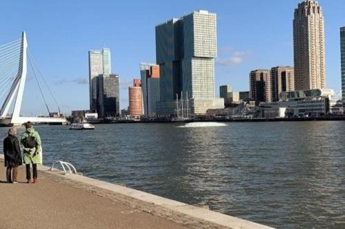 two people standing on a sidewalk near the water with a city at STUDIO ROTTERDAM Cntr in Rotterdam
