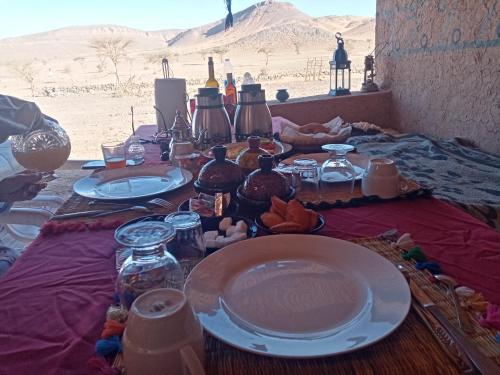 a table with plates and bottles on it in the desert at Auberge Camping Tafraoute Montagnes in Tafraoute Sidi Ali