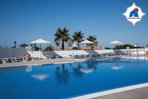 a large blue swimming pool with chairs and umbrellas at Costa do Vizir Beach Village in Porto Covo