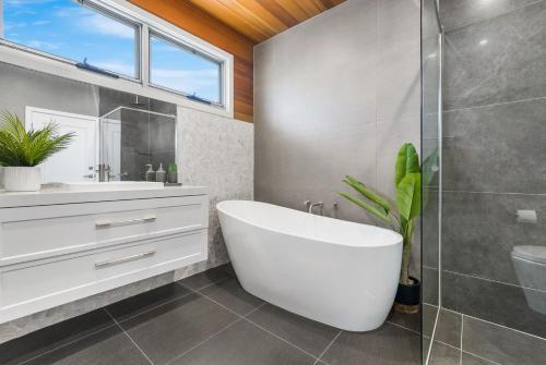 La salle de bains est pourvue d'une baignoire blanche et d'une douche en verre. dans l'établissement Surf Beach House, à Shellharbour