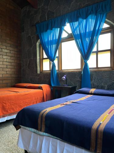 a bedroom with two beds with blue drapes at Casa Qatzij - Guest House, Lake Atitlan in San Lucas Tolimán