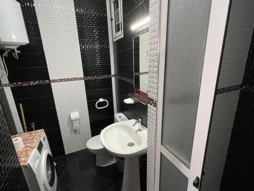 La salle de bains est pourvue d'un lavabo blanc et de toilettes. dans l'établissement Cité Jardins Appartement, à Martil