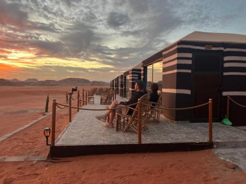 two people sitting outside of a building in the desert at Wadi Rum Desert Adventures in Wadi Rum