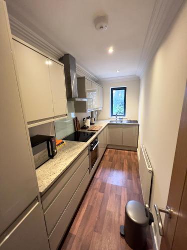 a small kitchen with white cabinets and wooden floors at Modern and cozy 2-guest flat with gated parking in Kingston upon Thames