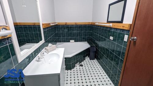 uma casa de banho com azulejos verdes, um lavatório e uma banheira em Nettin View 4 em Jindabyne