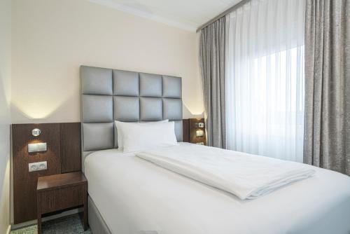 a bedroom with a white bed with a large window at NP Hotel Königshof in Dortmund