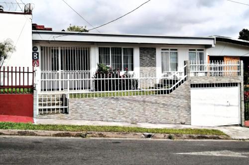 a house with a white fence on a street at Airport Traveler's home. in Alajuela City
