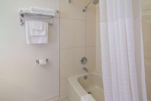 a bathroom with a tub and a shower with a white shower curtain at SureStay Hotel by Best Western North Vancouver Capilano in North Vancouver