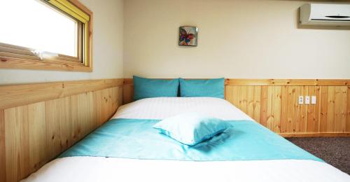 a bedroom with a bed with blue sheets and a window at Gotjawal Geomunoreum Pension in Jeju
