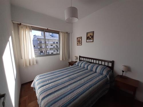 a bedroom with a bed with a striped comforter and a window at Depto Centro 2 amb para 2 o 3 personas Cochera in Mar del Plata