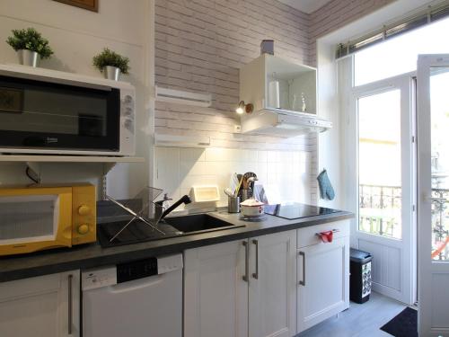 une cuisine avec un évier et un micro-ondes dans l'établissement Appartement T2 bis, balcon, 100m des thermes et commerces, WiFi, 4 pers, La Bourboule - FR-1-608-238, à La Bourboule