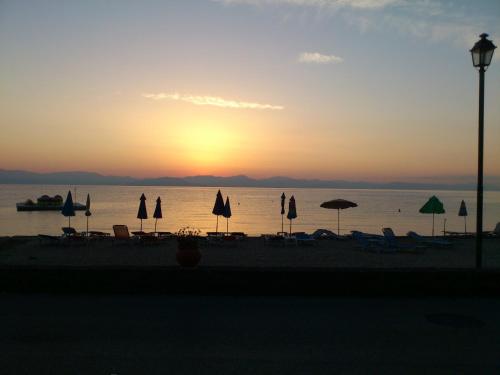 a group of umbrellas and chairs on the beach at sunset at Art Studios Benitses in Benitses