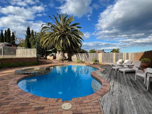 a backyard swimming pool with chairs and a palm tree at Summerhill Motor Inn in Merimbula