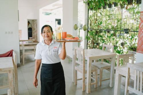 a woman holding a tray of food on a table at Bukal Sari Villas Uluwatu in Uluwatu