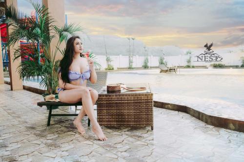 a woman in a bikini sitting on a bench next to a pool at Nest Resort in Pagudpud