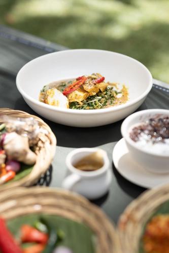 a table with a plate of food and a bowl of coffee at The Allure Ubud Villas & Spa crafted by freshWater Asia in Ubud