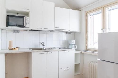 a white kitchen with a sink and a microwave at Upper floor studio with a sea view in Helsinki