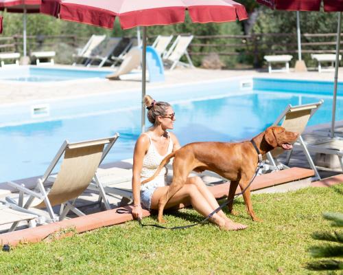 a woman sitting on a chair with a dog by a pool at Country Hotel Residence Da Pilade in Capoliveri