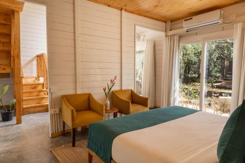a bedroom with a bed and two chairs and a window at LaRiSa Resort & Spa, Ashwem in Mandrem