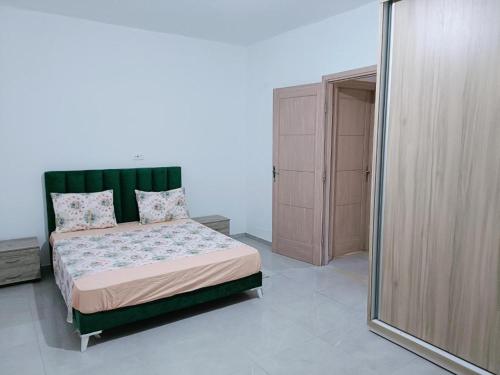 Schlafzimmer mit einem Bett mit einem grünen Kopfteil und einem Spiegel in der Unterkunft Family house in Ḩammām al Ghazzāz