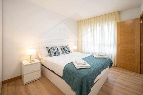 a white bedroom with a bed and a window at Ambar Playa San Lorenzo in Gijón