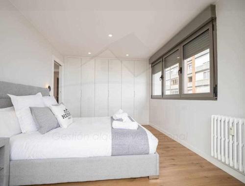 a white bedroom with a bed and a window at El Séptimo, Apartamento in Gijón