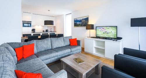 a living room with a gray couch and a tv at Residence Bellevue - incl Summercard in Zell am See