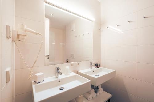 a white bathroom with two sinks and a mirror at Residence Bellevue - incl Summercard in Zell am See