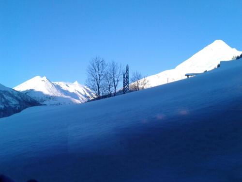 a snow covered hill with trees and snow covered mountains at Ferienwohnung Hohe Wand in Heiligenblut