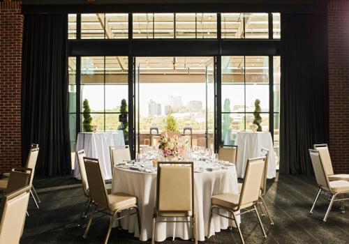 a dining room with white tables and chairs and windows at Archer Hotel Tysons in Tysons Corner