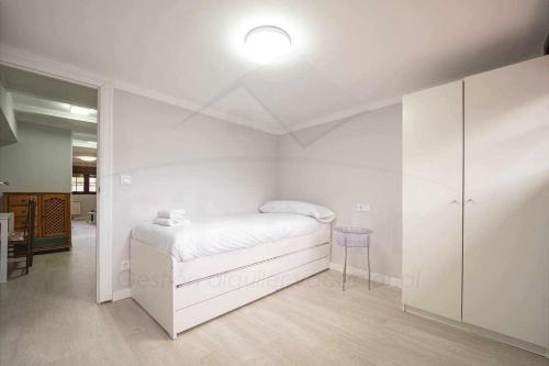 a white bedroom with a bed and a blue stool at El Pico, Apartamento in Ribadesella