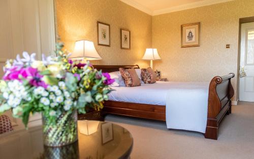 a bedroom with a bed and a table with a vase of flowers at Lucknam Park Hotel in Chippenham