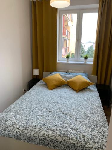uma cama com almofadas amarelas num quarto com uma janela em APARTAMENT GERSONA em Bydgoszcz
